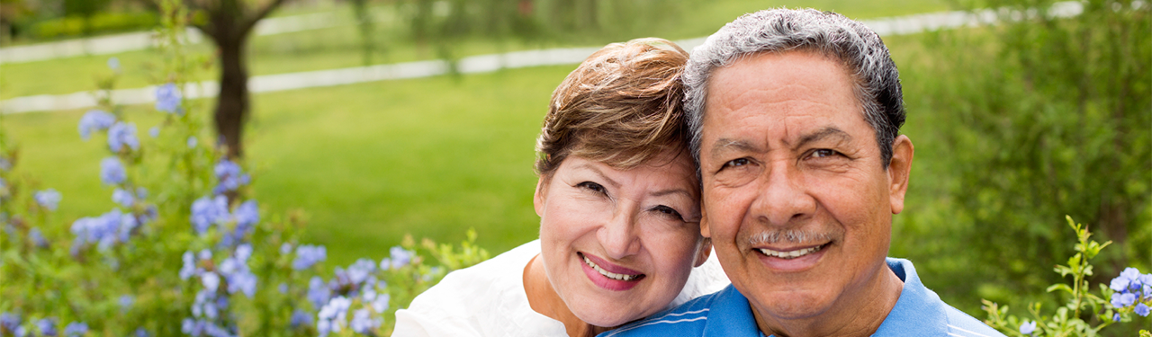 A headshot of a happy mature Latino couple outdoors by a garden.