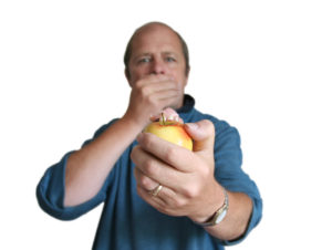 A man who bite into an apple and his dentures got stuck in the apple. He is covering his mouth in shock. 