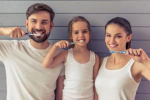 Beautiful parents and their daughter are looking at camera and smiling while brushing teeth 300x200 1