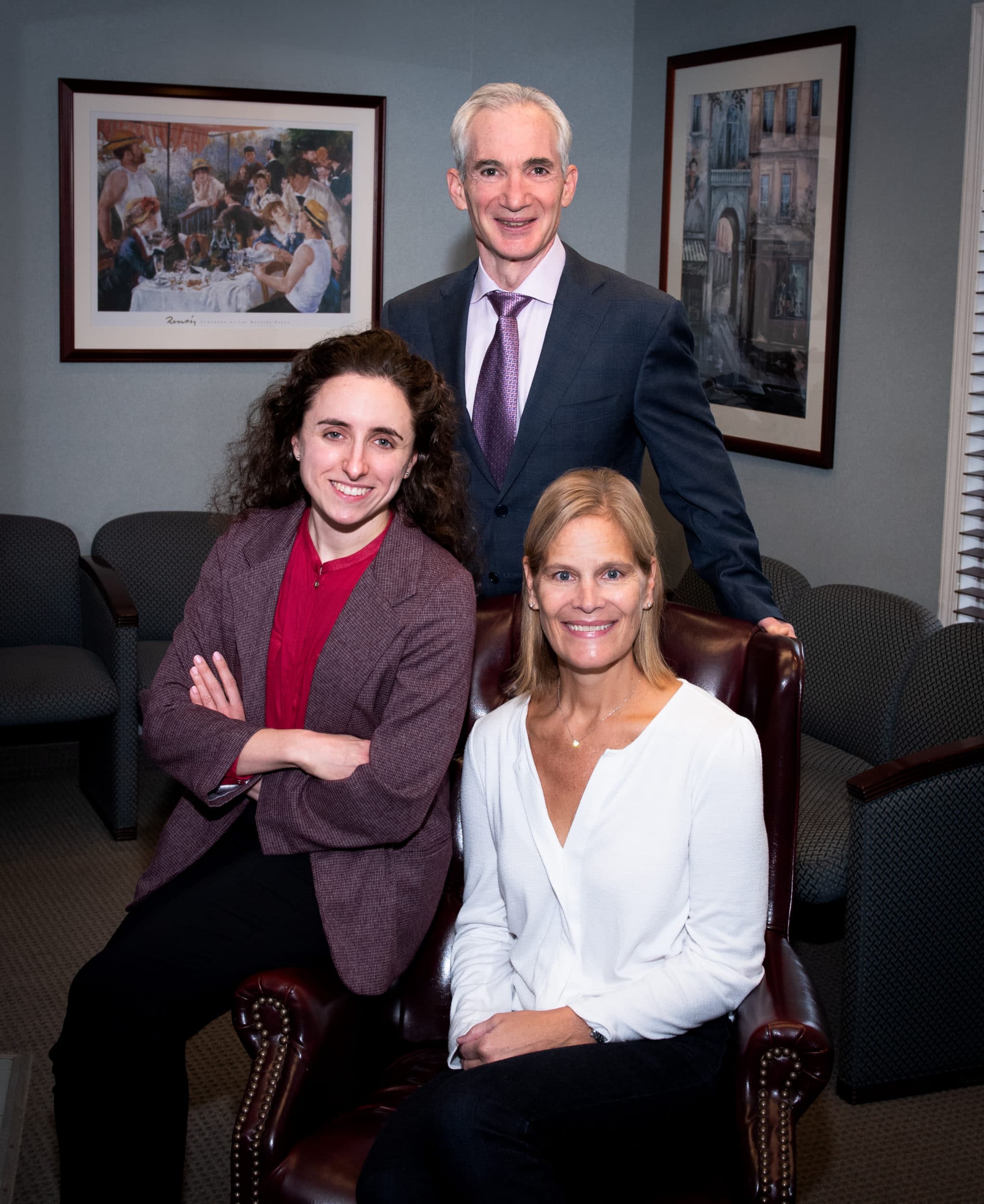 picture of main in suit with two woman seated in front of him in office smiling and posing for photograph