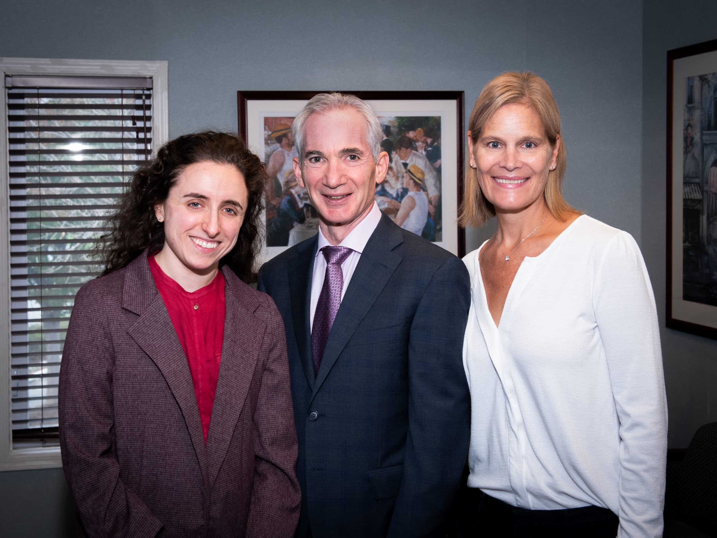 picture of main in suit with two woman on either side in office smiling and posing for photograph