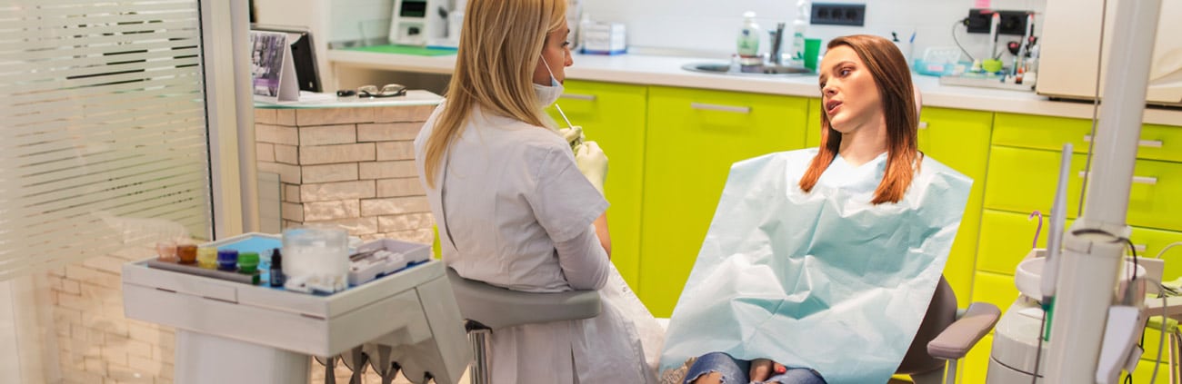 woman laying in dental office chait talking to dentist that is sitting beside her