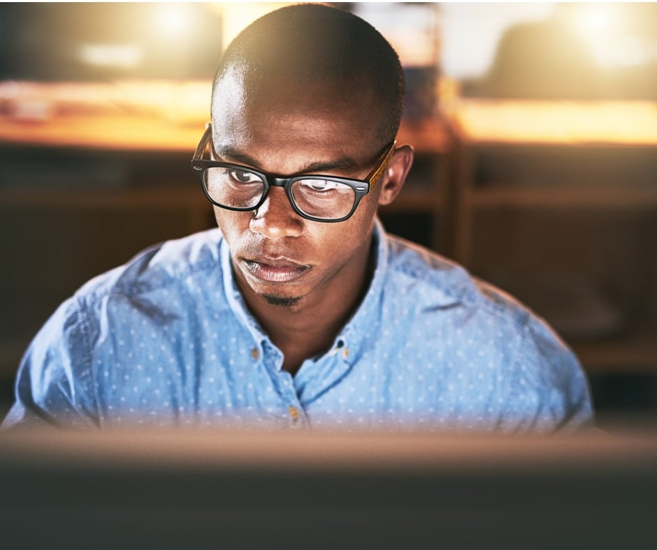 close up from behind the computer of a man with glasses looking at computer screen with blurry background