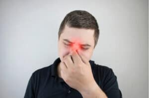 A man holds his nose with his hand and winces in pain.