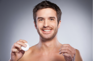 shirtless man holding dental floss and smiling