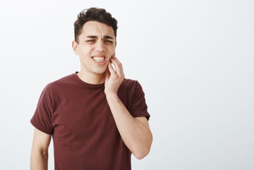 male in red t shirt frowning touching jaw while feeling toothache