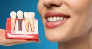 Young woman smiling as a dentist holds a dental implant model