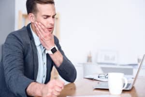 Man at work holding jaw in pain from TMJ