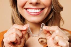 Woman smiling with beautifully straight teeth, holding a clear aligner in her hands