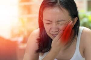 Woman holding her cheek and experiencing pain in her jaw from TMJ