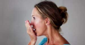 Woman with hand in front of mouth, smelling her breath.