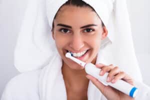 Woman brushing her teeth after a shower with an electric toothbrush