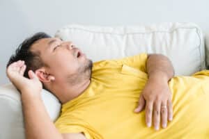 Man asleep on couch and snoring, due to sleep apnea.