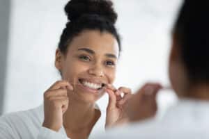 Woman smiling in the mirror while flossing, trying to prevent future issues with gum disease.