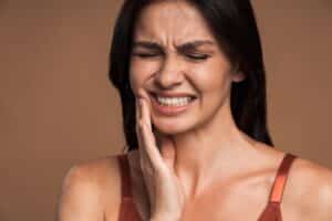 Young, beautiful woman clutching her jaw in pain from a cracked or broken dental crown.